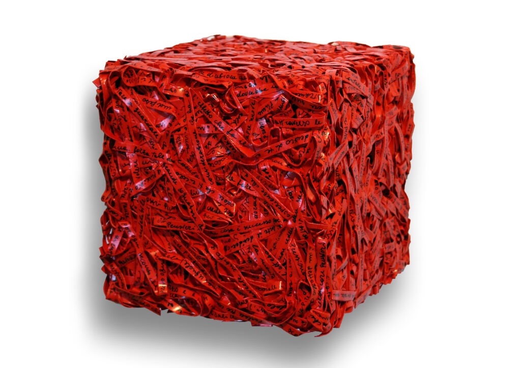 Parole in cubo 2017, scultura e opera d'arte contemporanea a tecnica mista di cm 20 x 20 x 20. L'opera si sviluppa tridimensionalmente a forma di cubo regolare, composta da un fitto e compatto intreccio materico di strisce di carta rossa con scritte e grafie manuali nere. Opera realizzata dall'artista Giovanni Fava.